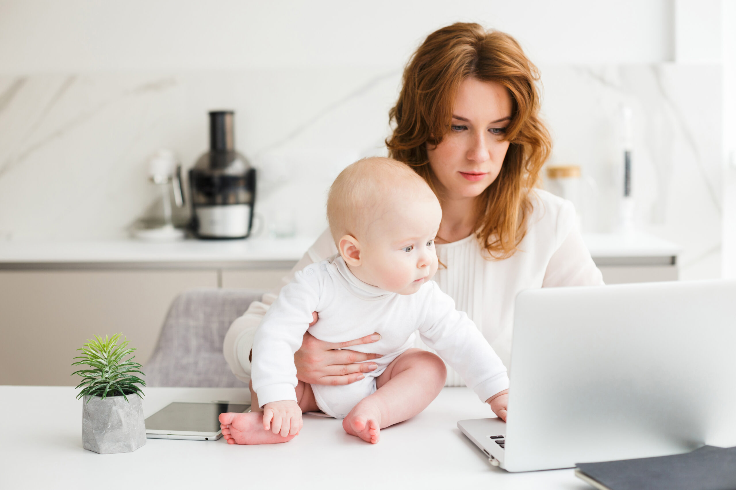 Thoughtful business woman working on laptop while holding her cute little baby near